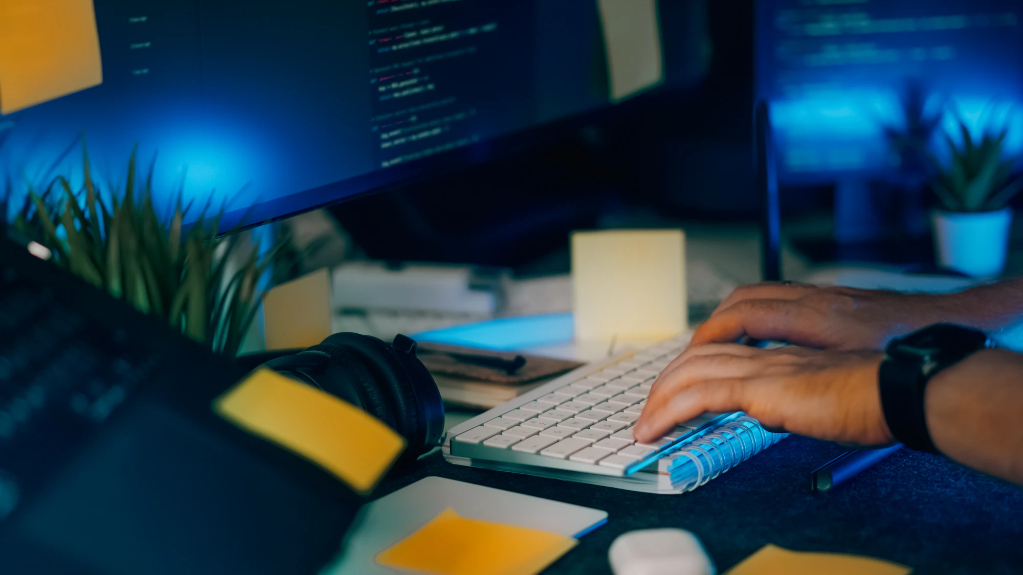 Manos trabajando frente a monitores con código desenfocado